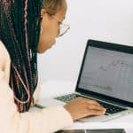 Woman in a Beige Jacket Analyzing the Graph on her Laptop